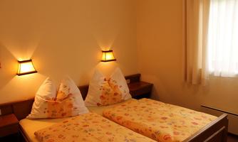 A cozy bedroom with two single beds and yellow bedcovers. Soft light from wall lamps creates a pleasant atmosphere.
