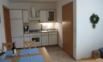 A modern kitchen with a wooden dining set and blue tableware. The walls are light, and there is a cabinet with glasses and dishes.