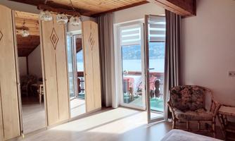 A bright room with wooden ceilings and large windows. The space is cozily furnished with an armchair and a view of a terrace.