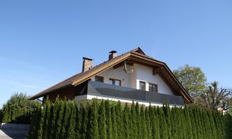 A beautiful house with a garden of tall cypress trees. The sky is clear and blue.