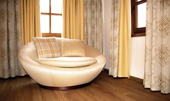 A modern beige sofa in a bright apartment. The windows are adorned with yellow curtains that create a warm glow.