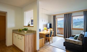 A bright and modern apartment with an open kitchen and a dining area. Large windows offer a view of the mountains.