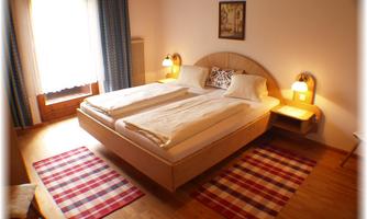 A cozy bedroom with a double bed and two nightstands. The room has wooden flooring and colorful rugs.