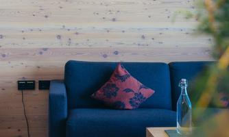 A cozy living room with a blue couch and a decorative pillow.  
On the wall, there is a modern lamp and a wooden table is in the foreground.