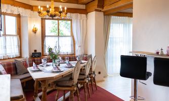An inviting dining area with a large wooden table and cozy chairs. Bright windows provide plenty of daylight and a warm atmosphere.