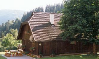 A traditional wooden house in the midst of nature. The garden is equipped with trees and a seating area.