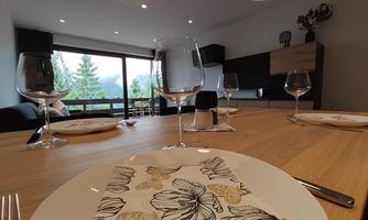 An elegant dining area with a wooden table and stylish glasses. In the background are large windows overlooking wooded mountains.