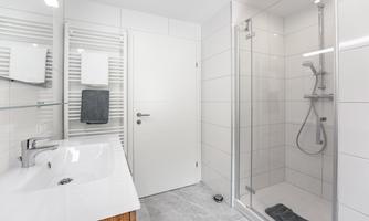 A modern bathroom with a spacious shower and an elegant vanity top. The walls are brightly tiled, creating a clean, minimalist ambiance.