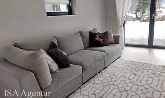 A cozy living room with a gray sofa and decorative cushions. The view from the window shows a winter landscape.