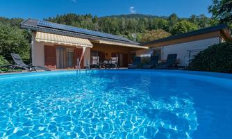 An inviting pool with clear water in front of a modern house. In the background, green trees and a blue sky can be seen.