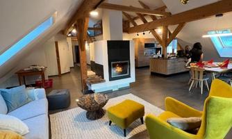 A cozy living room with modern furniture and a fireplace. The room has wooden beams and large windows that let in a lot of light.
