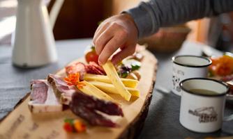 A rustic platter with sausage and cheese. A hand takes a piece of cheese from the platter.