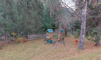 A playground made of wood is located in a dense forest. The ground is covered with fallen leaves.