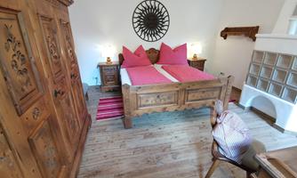 A cozy bedroom with a wooden bed and pink pillows. The room has a rustic style and a warm atmosphere.