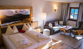A cozy hotel room with a double bed and a living area. Large windows provide daylight and a beautiful view of nature.