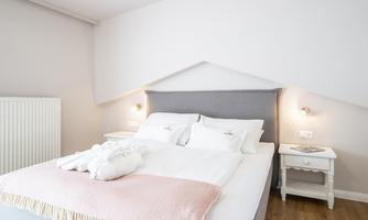 A modern bedroom with a large bed and a bright, friendly atmosphere. The walls are in soft colors, and there are nightstands next to the bed.