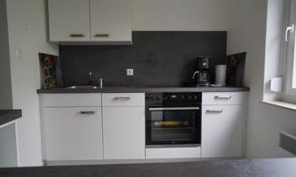 A modern kitchen with white cabinets and a dark countertop. It is equipped with a stove, a coffee machine, and a sink.