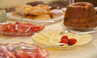 A table with various delicacies, including sausage, cheese, and fresh strawberries. In the background, pastries and a cake can be seen.