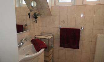 A modern bathroom with bright tiles and large windows. There is a sink, towels, and a small rolling cart.