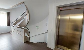 A bright staircase with a modern staircase and an elevator. Large windows let in plenty of light.
