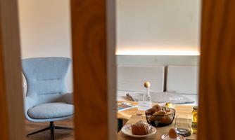 A bright room with a blue chair and a table set with breakfast dishes. On the table, there are rolls, eggs, and drinks.