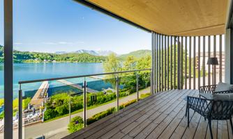 A beautiful view from a balcony of a quiet lake and green hills. The weather is sunny with a clear sky.