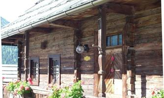 A rustic wooden house with traditional shutters and a well-maintained balcony. Colorful flowers adorn the windows and the outdoor area.