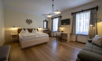 A bright, modern bedroom with a double bed and a cozy sofa. Large windows provide plenty of natural light and a pleasant atmosphere.