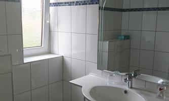 A bright bathroom with white tiles and a large mirror. There is a window that lets in natural light.