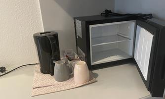A kettle and a small fridge are standing next to two cups on a table. The fridge is open and empty.
