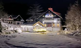 A picturesque building at night, surrounded by snow. It radiates warm light and reflects in the calm water.