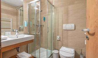 A modern bathroom with a glass shower and a wooden sink. The walls are tiled beige, and fresh towels are visible.