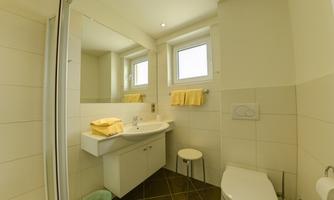 A modern bathroom with bright tiles and a large mirror. There is a sink, a shower, and a toilet, as well as fresh towels.