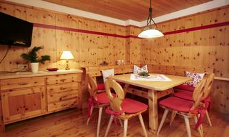 A cozy dining area made of wood with a round table and red chairs. There is a TV on the wall, and an elegant lamp provides warm light.