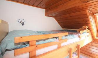 A cozy wooden loft bed in a room with wooden ceilings. The bed is decorated with a colorful bedding set and a plush toy.