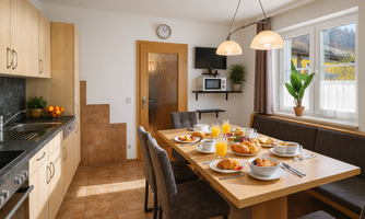 A bright kitchen with a large table set for breakfast. In the background, there are kitchen cabinets and a plant.