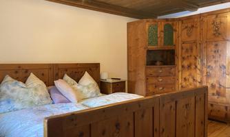 A cozy bedroom with a wooden bed and a large wardrobe. The walls are in warm wood tones, and there are soft cushions on the bed.