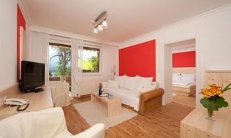 A modern living and bedroom with red accents and bright furniture. Large windows provide plenty of daylight and an inviting atmosphere.