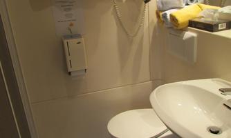 A small bathroom with a sink, a toilet, and a shower area. Towels in yellow and blue are neatly hung.