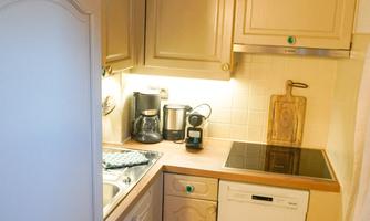 A small, modern kitchen with light cabinets and a practical layout. It features a stove, a dishwasher, and kitchen utensils.