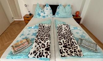 A bedroom with a large bed, decorated with blue and white stars and animal patterns. On the bed are folded towels and blankets.
