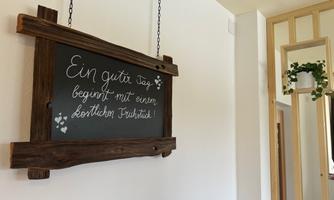 A handcrafted wooden sign hangs on the wall. It displays the text: "A good day begins with a heartfelt kindness."