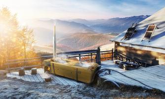 A cozy mountain cabin in an autumn landscape. In the foreground, there is a wooden stove emitting smoke, and the mountains are visible in the background.