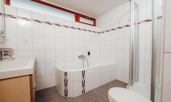 A modern bathroom with a bathtub and a separate shower cabin. The walls are tiled in white, and there are wooden details.