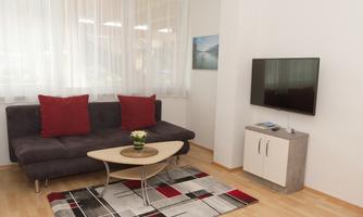 A modern living room with a cozy sofa and red cushions. The TV is mounted on the wall, and an elegant table complements the decor.