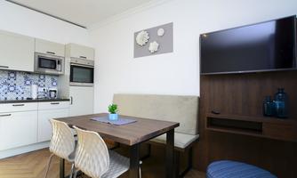 A modern kitchen with a dining area and a television. The room is bright and friendly designed.