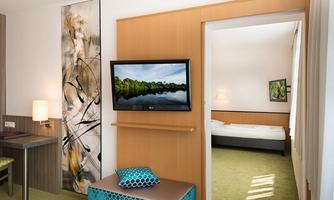 A modern room with a television and a stylish seating area. Through the room, you can see another bedroom with a cozy bed.