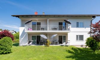 A modern house with two floors and two balconies. The well-kept garden is green and inviting.