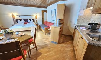A cozy room with a double bed, a red couch, and a dining table. The modern kitchen is well-equipped and the wooden floor creates a warm atmosphere.