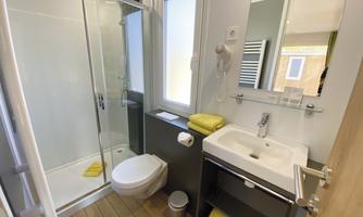 A modern bathroom with a shower, sink, and toilet. Yellow towels and wooden flooring create an inviting atmosphere.